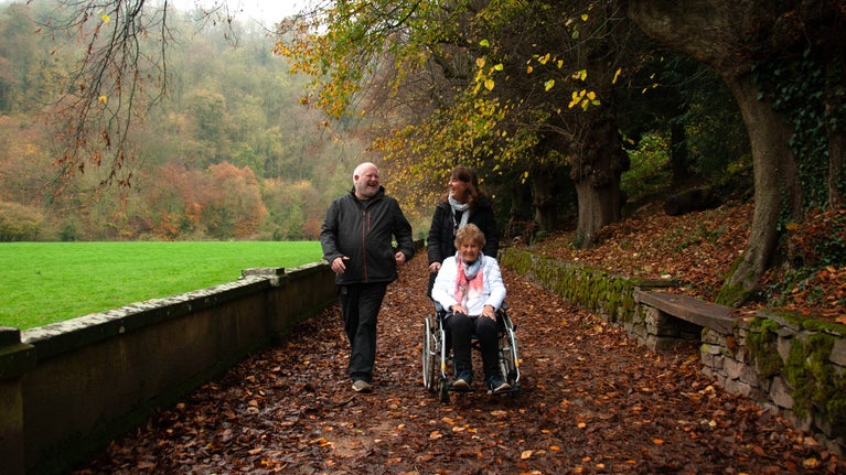 A woman being pushed in a wheelchair by another woman, with a man walking alongside them.